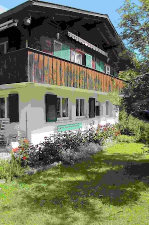 A two-story building with a balcony, a garden with flowers, and a bench. - Helene Appartement/Fewo, Dusche, WC, 2 Schlafräume 3-Zimmerwohnung Parterre by Interhome (Adelboden)