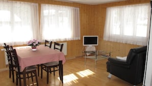 Een kamer met een eettafel, stoelen, een televisie en een bank.