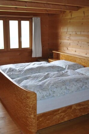 Een houten kamer met een bed, een raam met gordijnen en een houten bank.