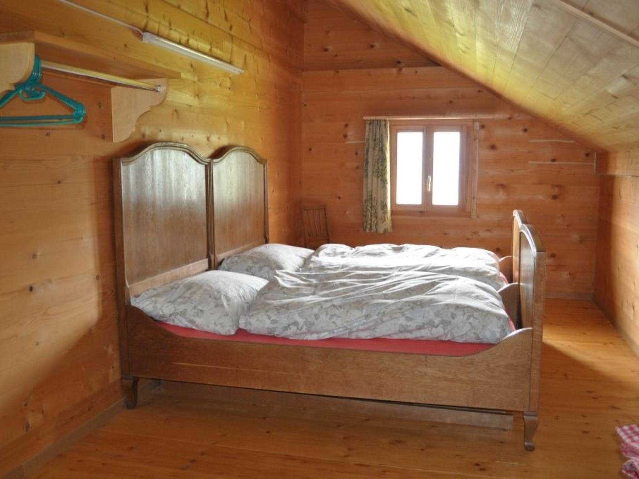 Ein Schlafzimmer einer Holzhütte mit einem Einzelbett, einem Fenster und einer Holzbalkendecke.