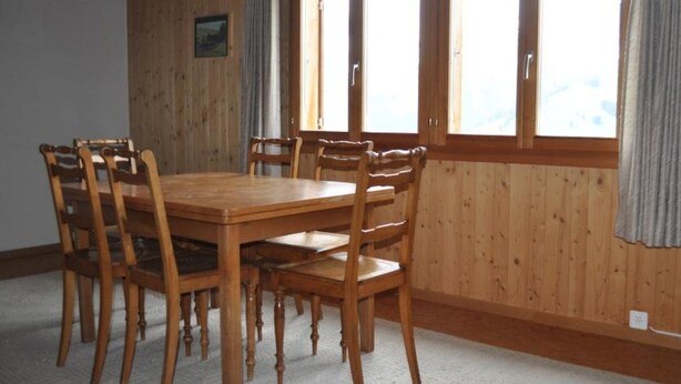 A wooden dining table with six chairs, large windows with curtains, and a picture on the wall. - Sennhütte Gibeli Hütte, Bad, WC, 4 oder mehr Schlafräume Sennhütte by Interhome (Frutigen)