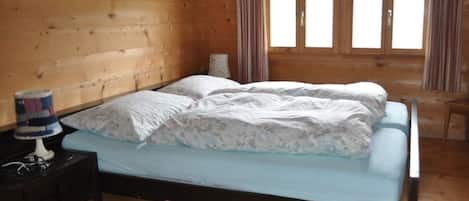 Una habitación de cabaña de madera con una cama, una mesita de noche y una ventana con cortinas.