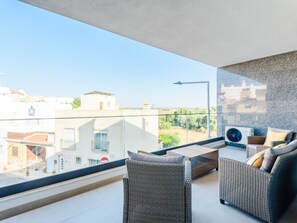 Ein Balkon mit Korbmöbeln, Blick auf Gebäude und bewölkter Himmel.
