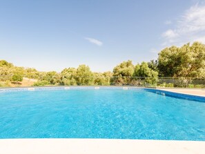 Ein klares, blaues Schwimmbecken, umgeben von einem Zaun, mit Bäumen und einem wolkenlosen Himmel im Hintergrund.