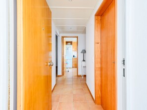 Um corredor com portas de madeira e chão de azulejos, que leva a uma cozinha com armários e uma geladeira.