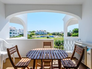 Ein Balkon mit einem Holztisch und Stühlen, der auf einen Wohnbereich mit Gebäuden und Grünflächen blickt.