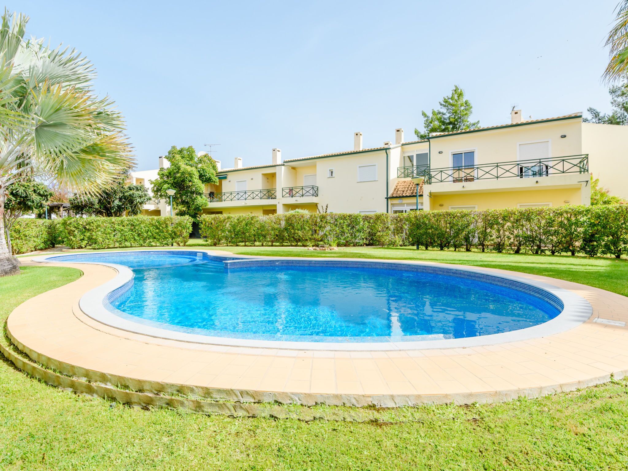 Uma piscina com design curvo, cercada por um gramado bem cuidado e uma fileira de edifícios residenciais ao fundo.