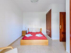 A hotel room with a wooden bed, a nightstand, a lamp, and a wardrobe. - Apartment  by Interhome (Vilamoura)