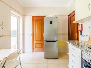 A modern kitchen with a stainless steel refrigerator, wooden cabinets, and a dining area with a chair. - Apartment  by Interhome (Vilamoura)