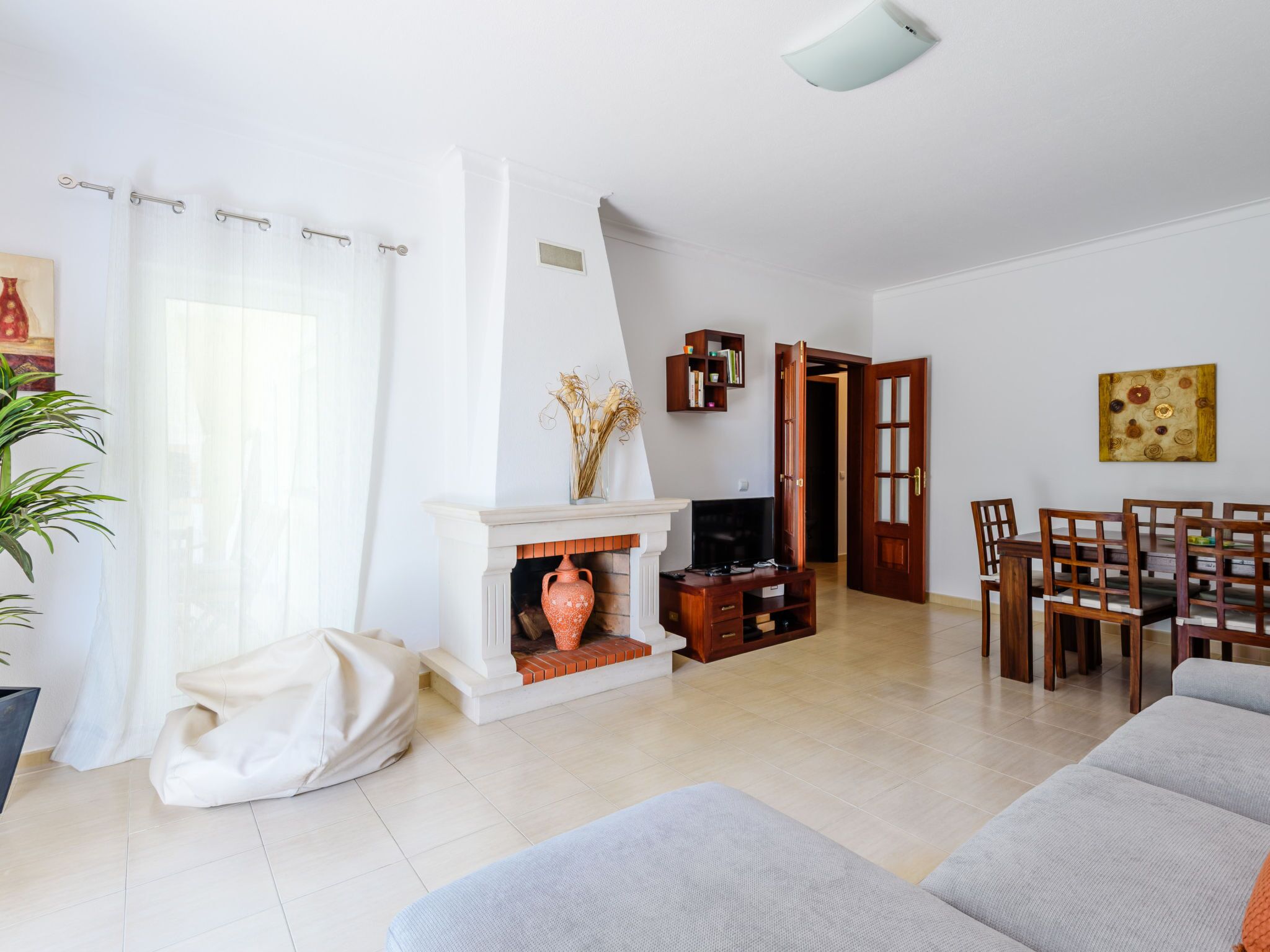 A living room with a fireplace, a sofa, a dining area with chairs, and a bookshelf.