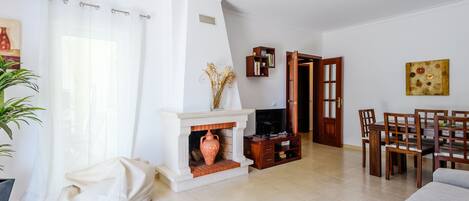 A living room with a fireplace, a sofa, a dining area with chairs, and a bookshelf.