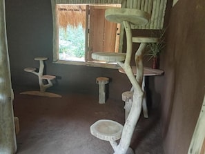 Una habitación con un rascador para gatos, una ventana que da a zonas verdes y una mesita.