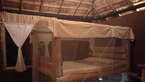Un lit simple avec une moustiquaire, des murs en bois et un toit de chaume.