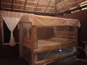 A single bed with a mosquito net, wooden walls, and a thatched roof. - Nature Kingdom Sri Lanka (uva province)
