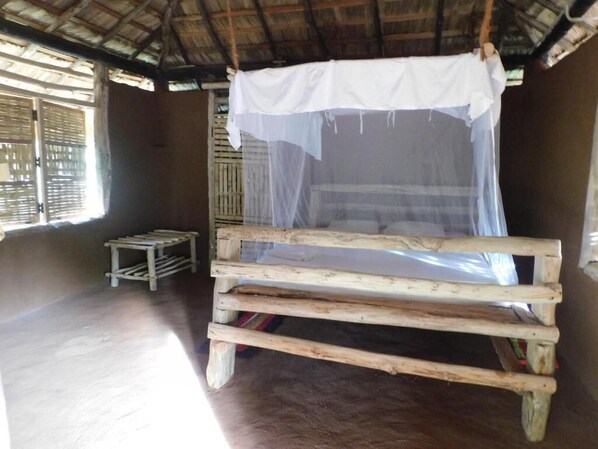 A simple wooden bed with a mosquito net in a room with a thatched roof and wooden walls. - Nature Kingdom Sri Lanka (uva province)