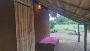 Une cabane rustique avec un toit de chaume, une porte en bois et un petit lit recouvert d’une couverture colorée.