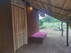 A rustic hut with a thatched roof, a wooden door, and a small bed with a colorful blanket. - Nature Kingdom Sri Lanka (uva province)