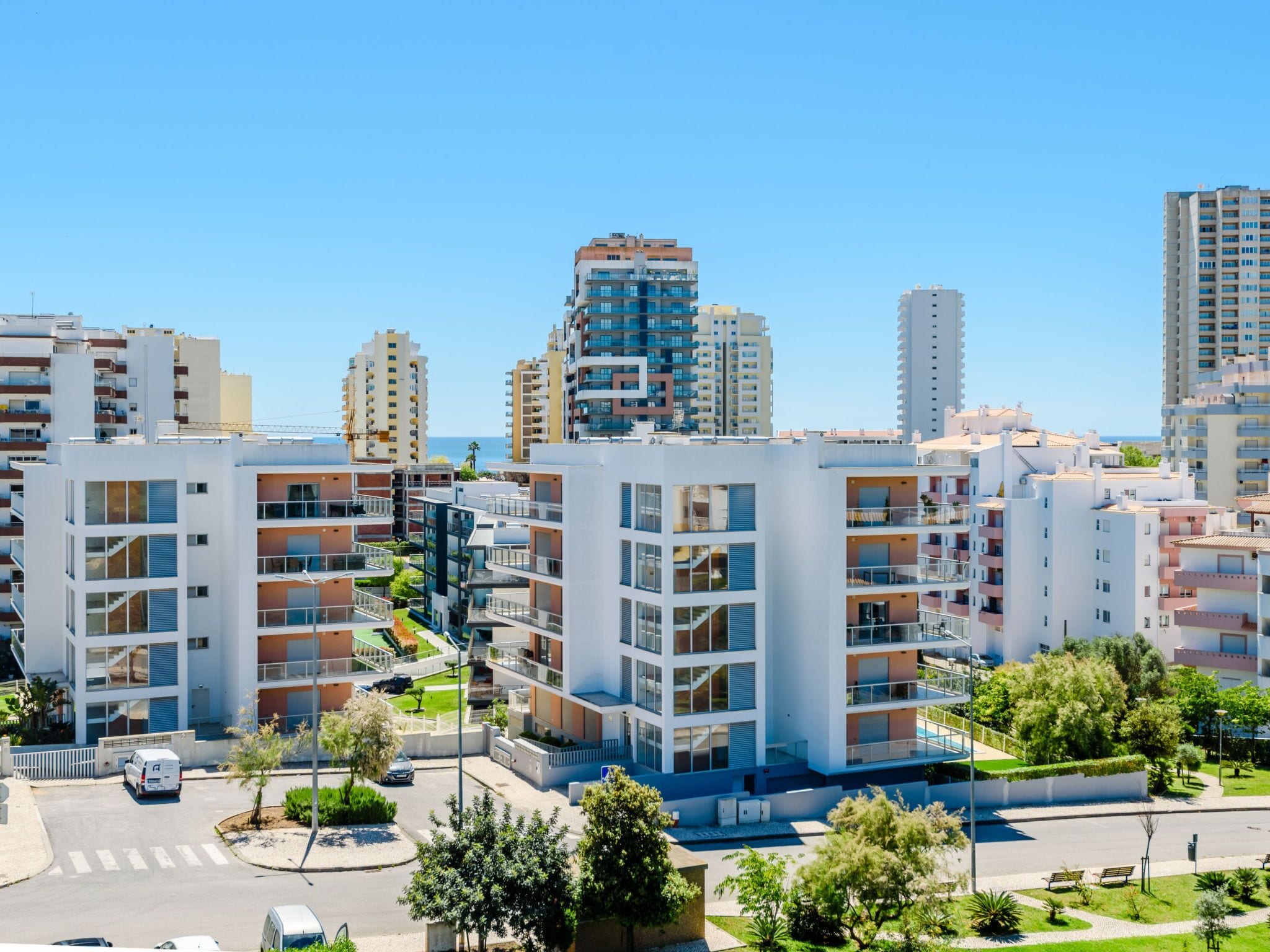 A modern residential area with multi-story apartment buildings, a clear sky, and a road with vehicles.