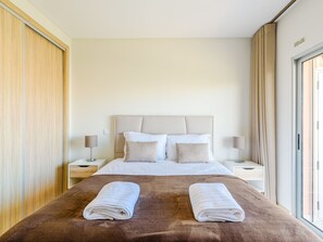Ein Hotelzimmer mit einem großen Bett, zwei Nachttischen, einer Kopfteil und Blick durch ein Fenster.