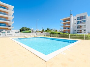 A swimming pool with a tiled deck, surrounded by a white fence, with modern buildings in the background. - Apartment  by Interhome (Praia da Rocha)
