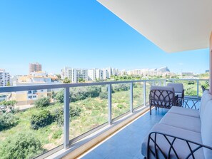 Ein Balkon mit Blick auf eine Stadtlandschaft, eine Sitzecke mit Sofa und zwei Stühlen.