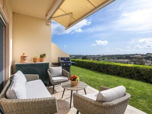 Eine Terrasse mit Korbmöbeln, einem Grill und Blick auf eine Stadt.