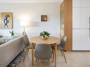 Ein modernes Wohnzimmer mit einem runden Holztisch, grau gepolsterten Sesseln, einer Couch, einer Stehlampe und einem Blumentopf.