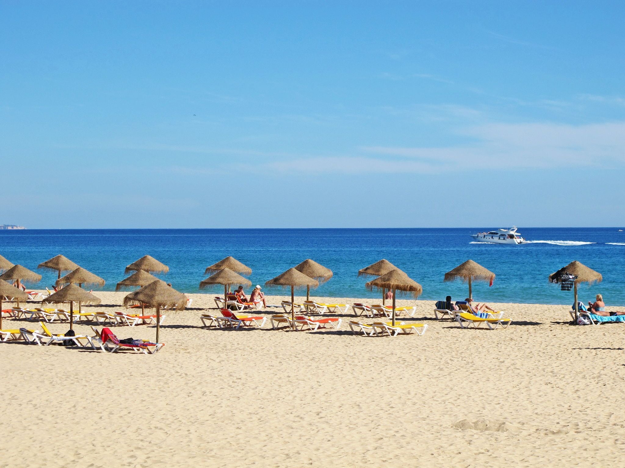 A beach with rows of sun loungers and thatched umbrellas.