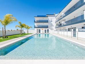 A modern building with a swimming pool, multiple balconies, and a clear blue sky. - Apartment  by Interhome (Tavira)