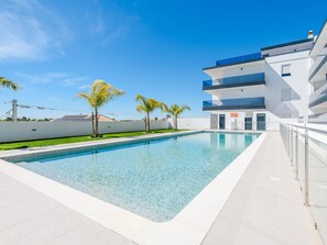 Um edifício moderno com piscina, céu claro e palmeiras.