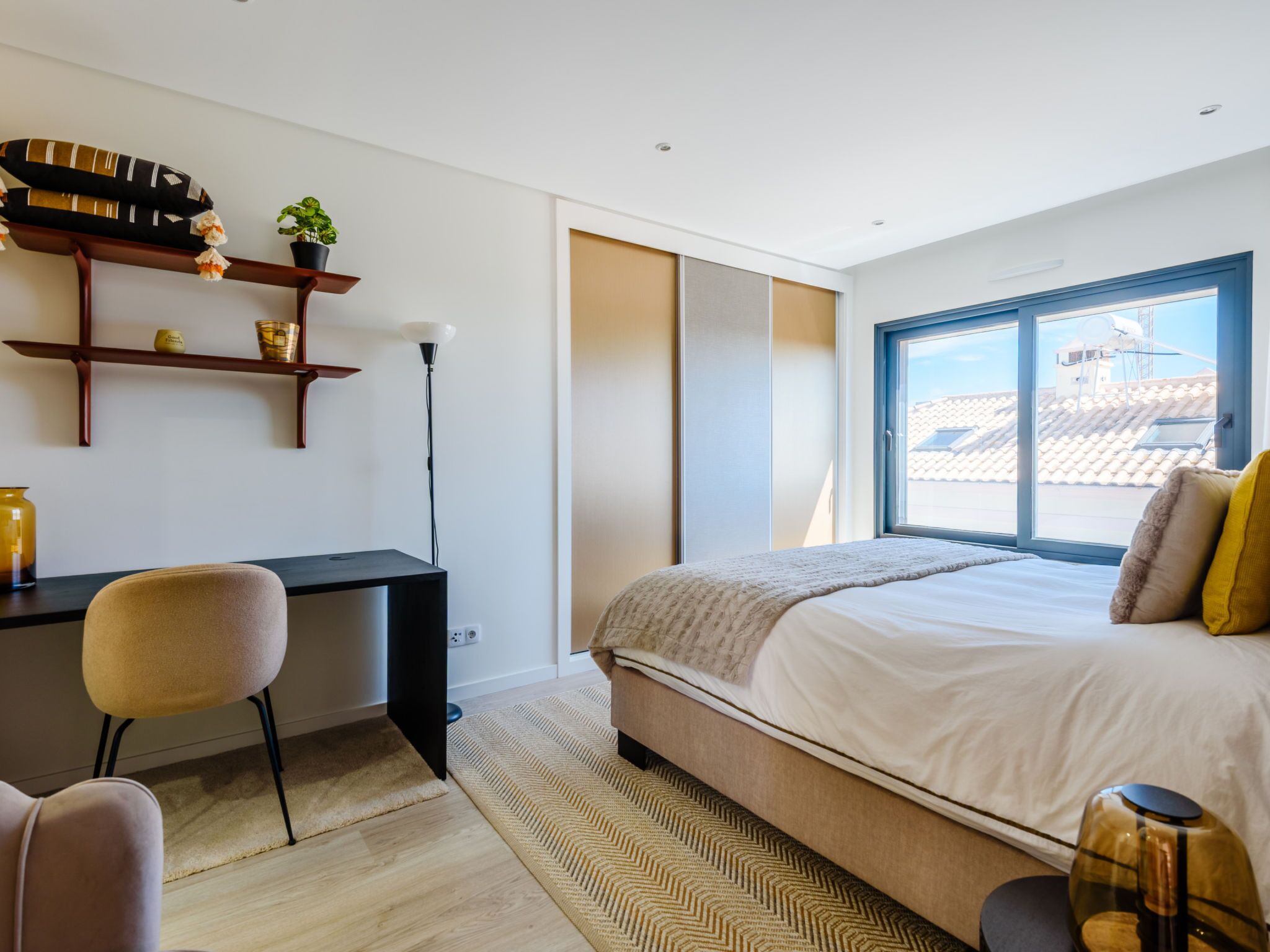 A modern bedroom with a bed, desk, chair, and a view of the outside.