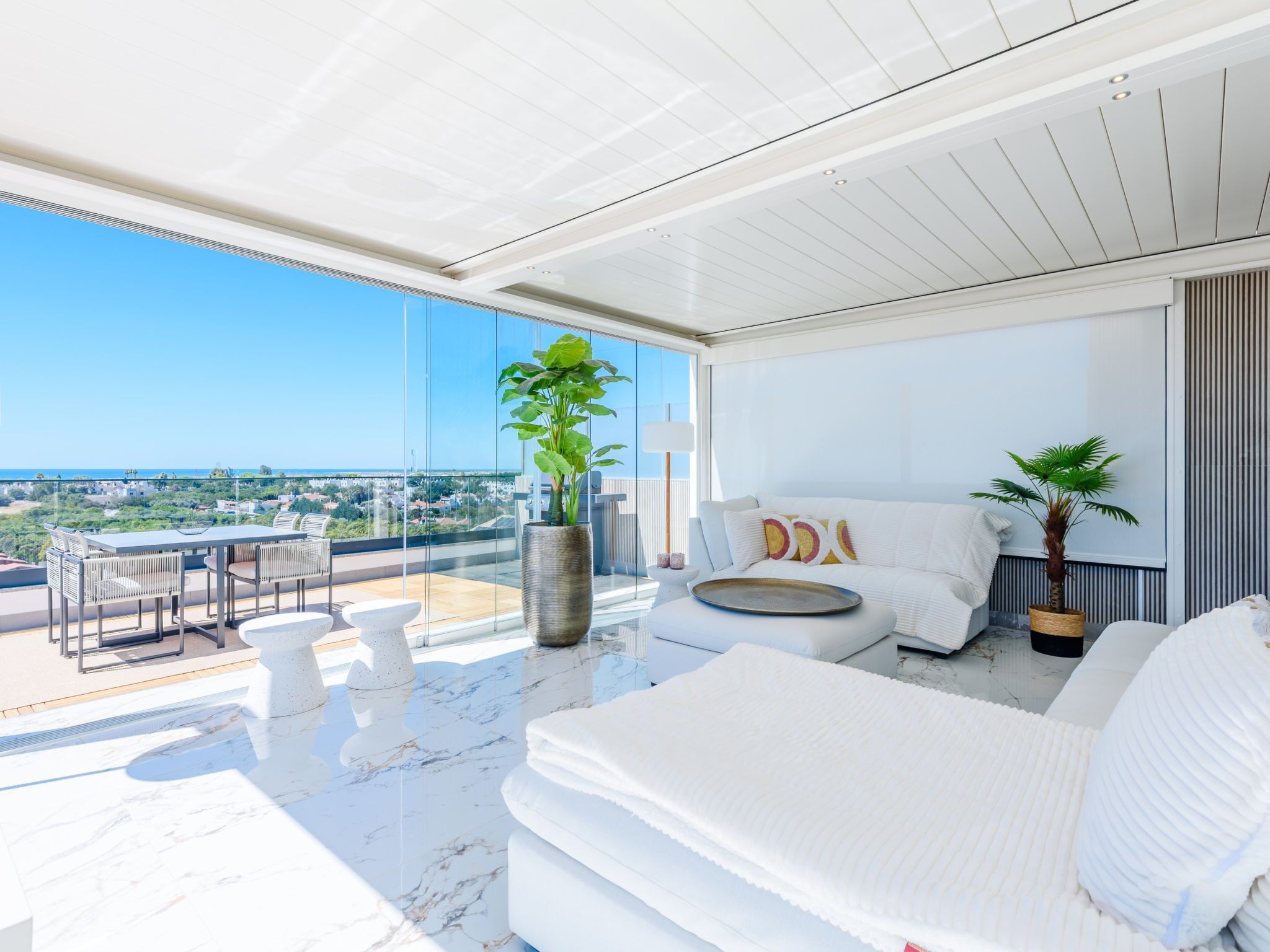 A modern living room with a large window, a sofa, a dining area, and a view of the city.