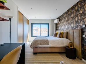 Quarto moderno com uma cama grande, uma escrivaninha e vista para a paisagem urbana pela janela.