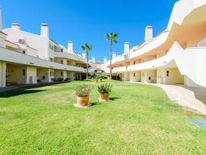 A courtyard with a central lawn, potted plants, and a clear blue sky. - Apartment  by Interhome (Vale do Lobo)