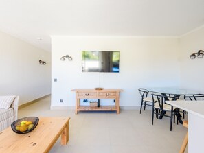 A modern living space with a wooden dining table, a glass-top dining table, and a sofa. - Apartment  by Interhome (Vale do Lobo)