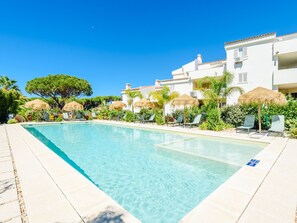 A clear swimming pool with lounge chairs and umbrellas, surrounded by greenery and white buildings. - Apartment  by Interhome (Vale do Lobo)