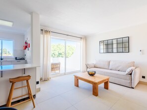 A modern living room with a sofa, a coffee table, and a kitchen area with a counter and stools. - Apartment  by Interhome (Vale do Lobo)
