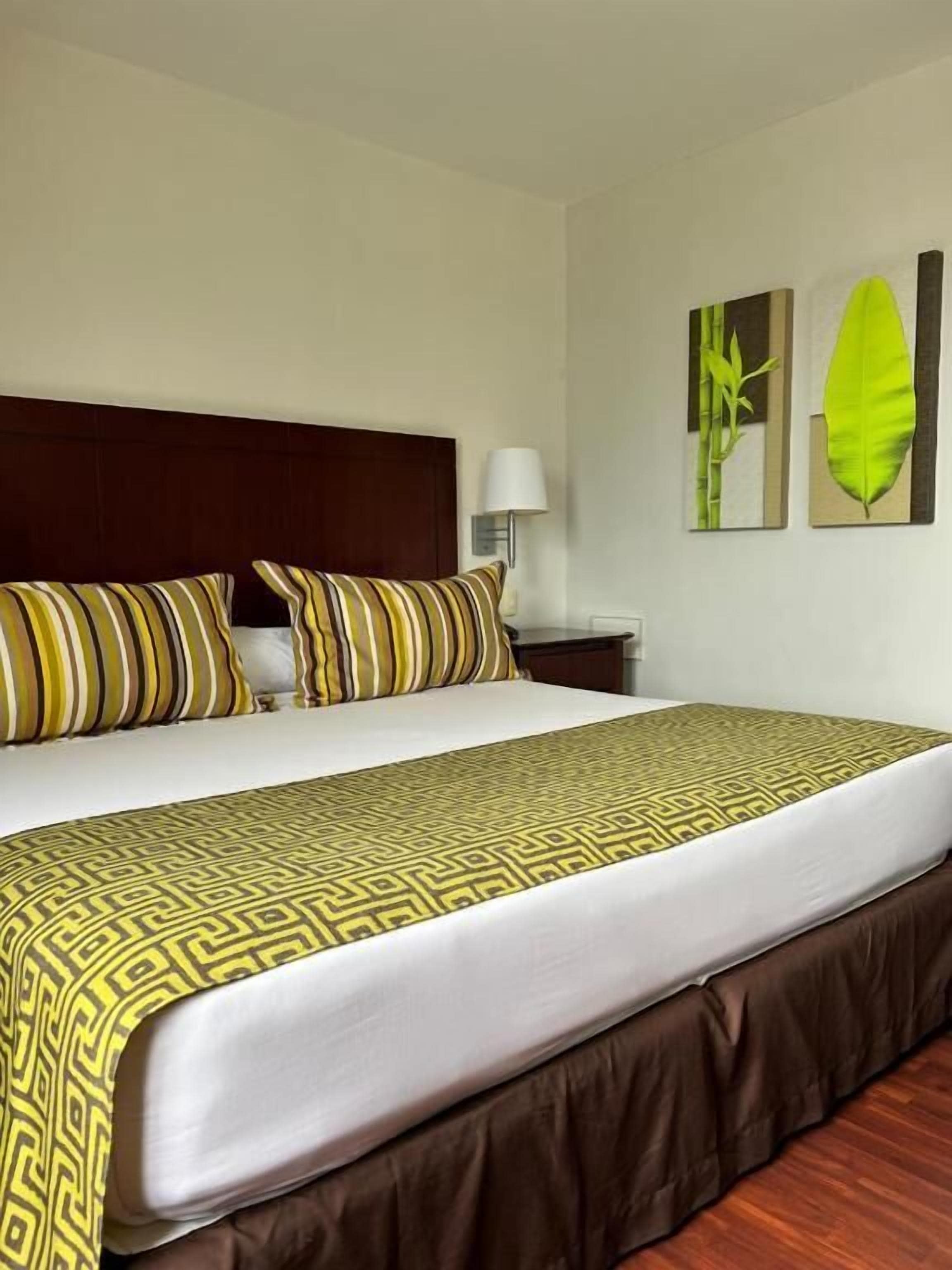 A hotel room with a bed, a nightstand, and wall art.