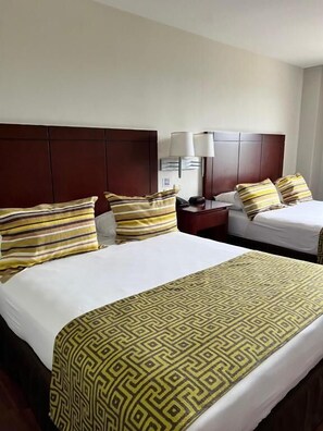 A hotel room with two beds, each with a patterned bedspread and pillows. There is a nightstand with a lamp between the beds.