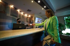 A reception desk with a computer monitor, a person handing over a card, and a plant in the background. - Hotel GH Guaparo Inn Valencia (Naguanagua)