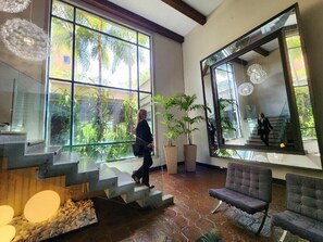 A modern interior with a staircase leading to a balcony, large windows, and indoor plants. - Hotel GH Guaparo Inn Valencia (Naguanagua)