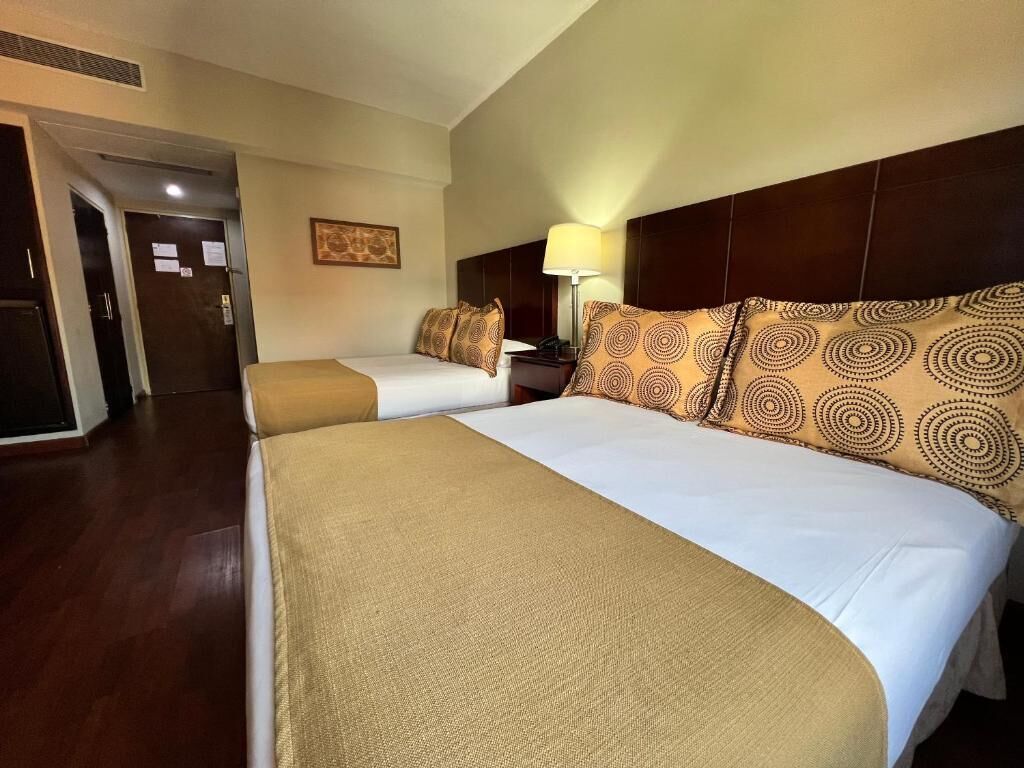 Una habitación de hotel con dos camas, cabeceros, mesitas de noche y lámparas.