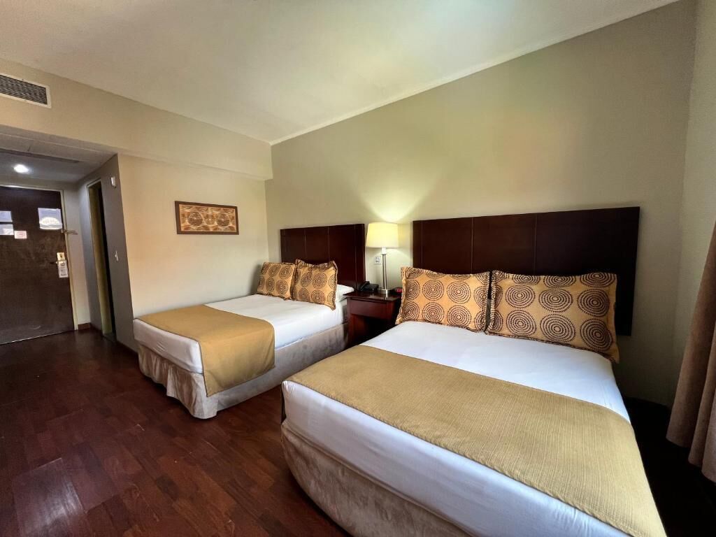 Una camera d'albergo con due letti, un comodino, una lampada e una porta.