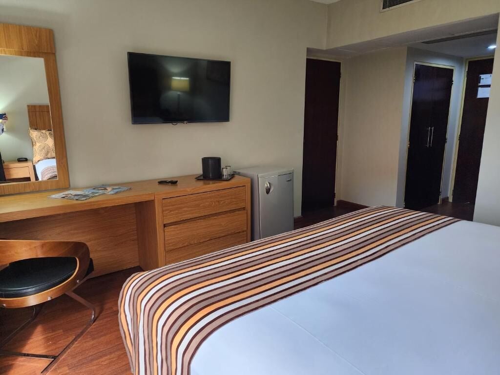 A hotel room with a bed, a desk, a chair, a television, and a door.