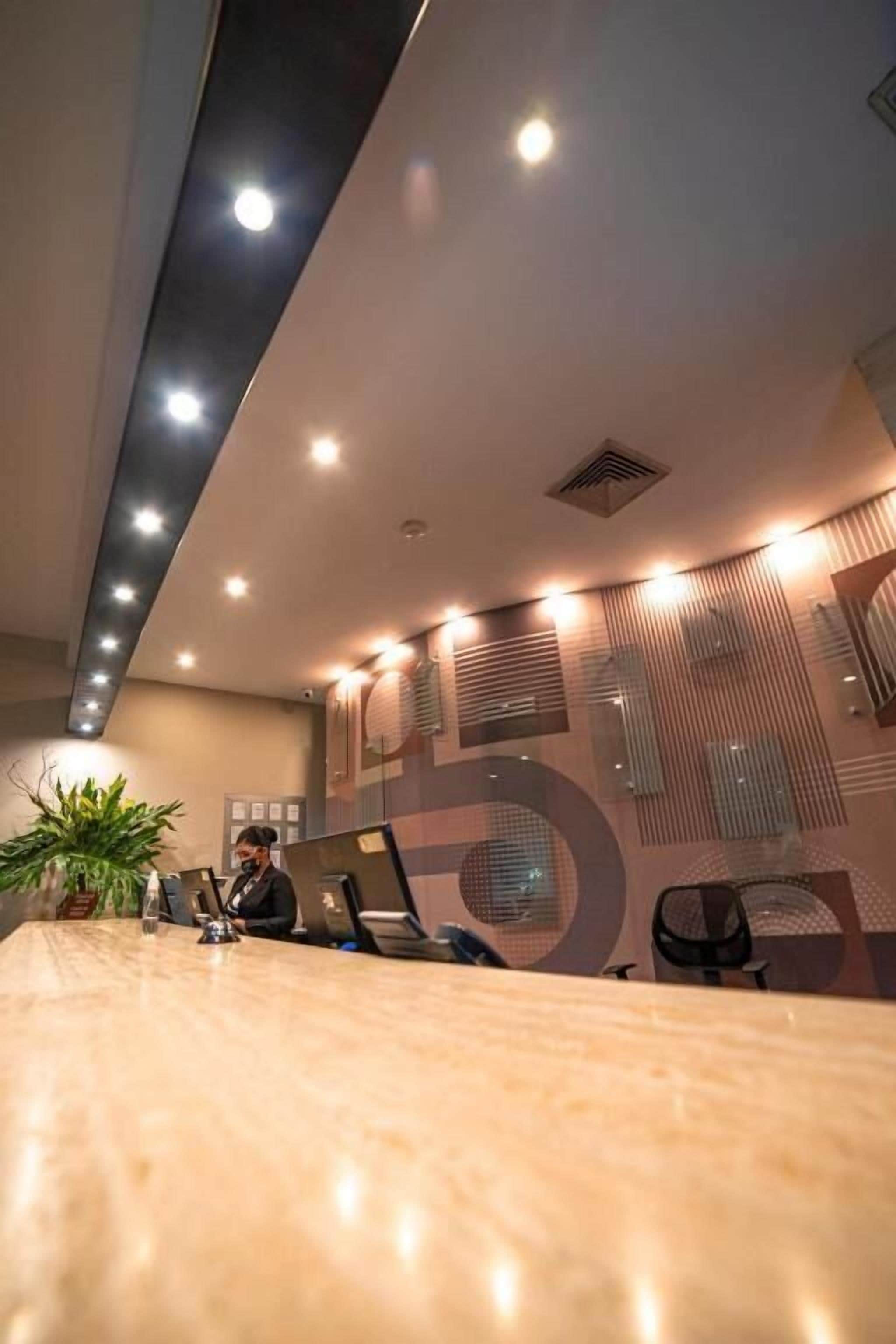 Un interno ufficio moderno con un lungo tavolo da conferenza, diverse sedie e una persona al lavoro a una scrivania.