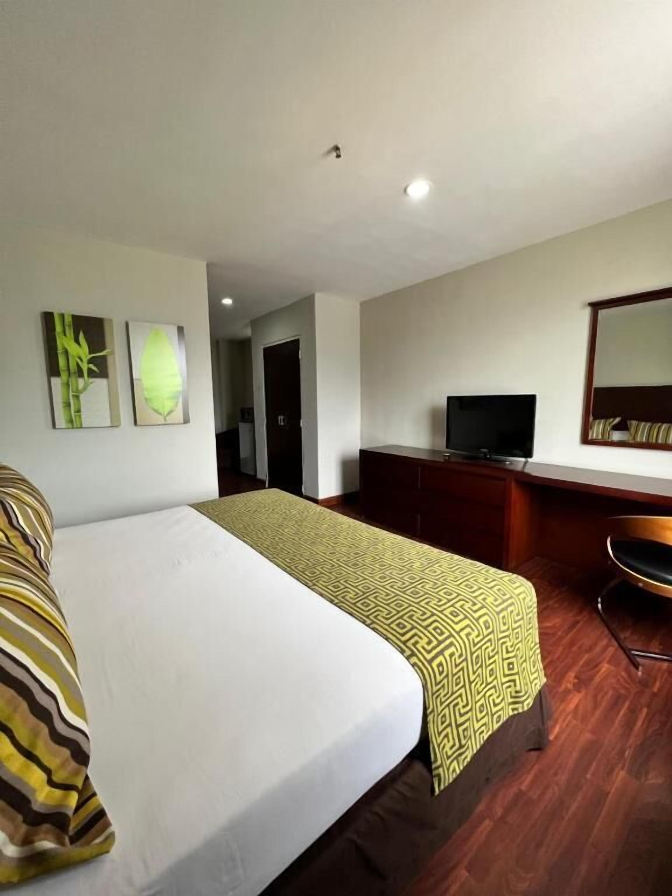 Una camera d'albergo con un letto, una scrivania con televisore e uno specchio.