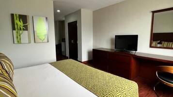 Una camera d'albergo con un letto, una scrivania con televisore e uno specchio.