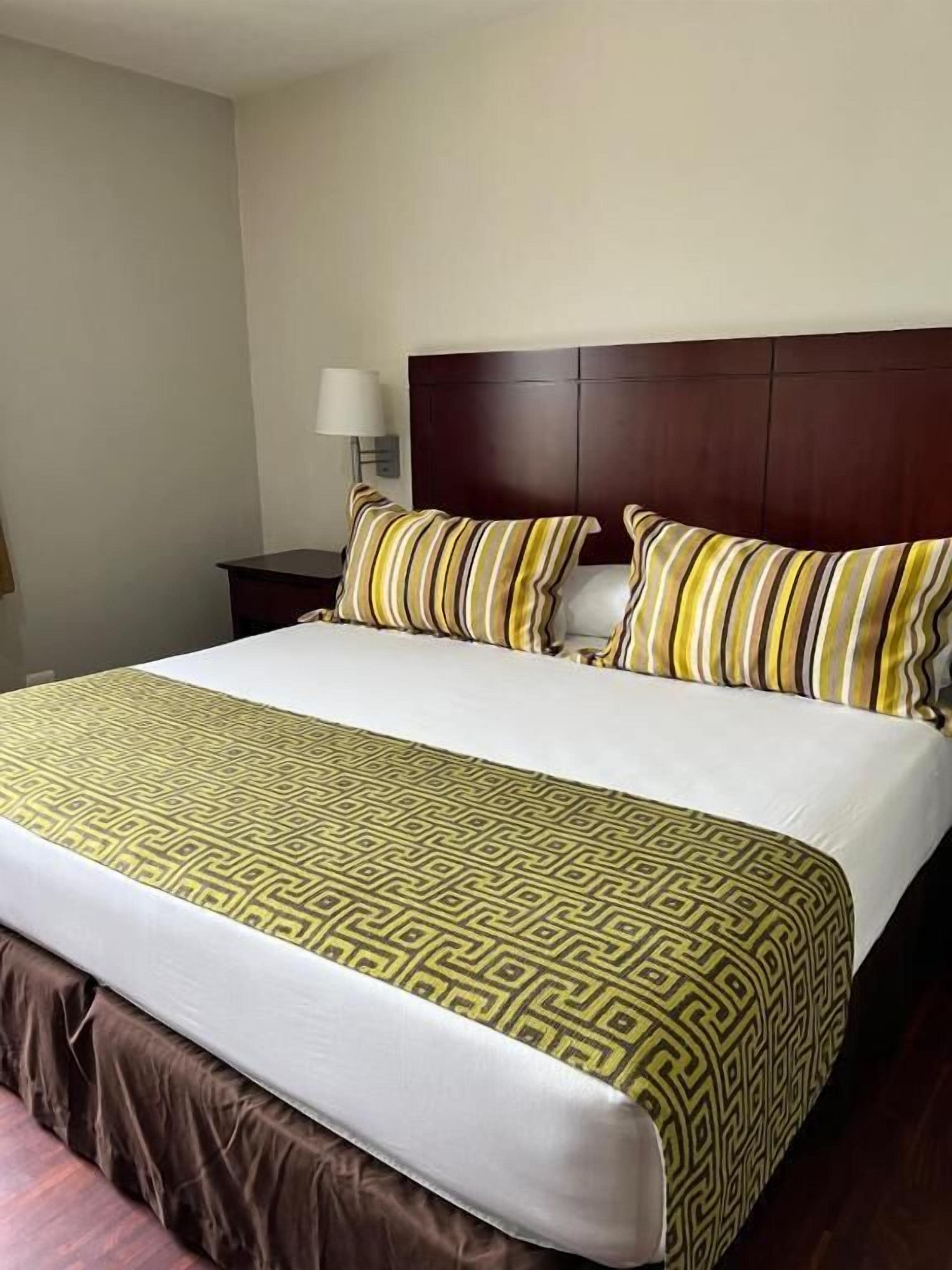 Een hotelkamer met een groot bed, een houten hoofdbord, een nachtkastje en een lamp.