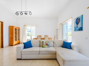 Un salon moderne avec un canapé d’angle, un meuble en bois et un coin repas avec des chaises.
