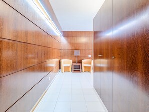 Ein Korridor mit Holzwandverkleidung, Fliesenboden und zwei Stühlen an einem kleinen Tisch mit einer Lampe.